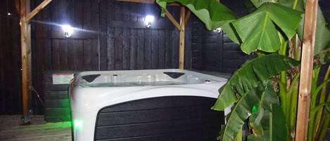 Un jacuzzi en una estructura de madera, con interior oscuro y plantas verdes.