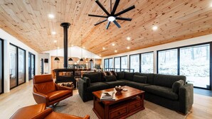 A spacious living area with a large sectional sofa, a leather armchair, and a wooden coffee table. A modern ceiling fan and a fireplace are visible. - Luxury Mountain Retreat: Skiing, Hiking, Sauna (Tucker County)