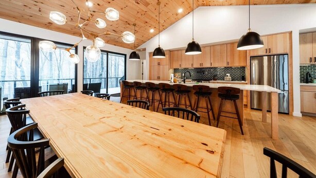 A modern kitchen with wooden cabinets, a stainless steel refrigerator, and a large island with bar stools. - Luxury Mountain Retreat: Skiing, Hiking, Sauna (Tucker County)