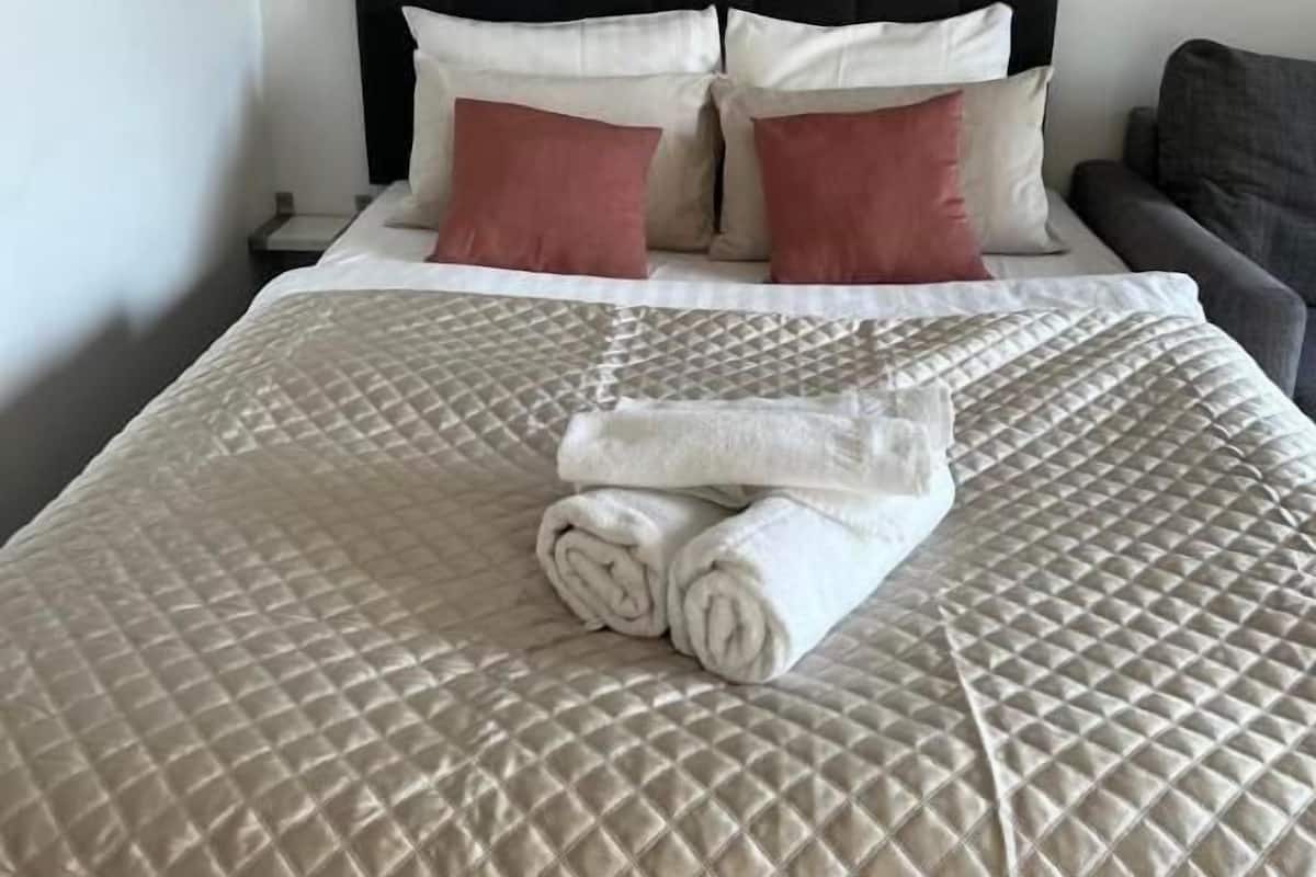 A neatly made bed with a quilted cover, two pillows, and a rolled towel on a headboard.