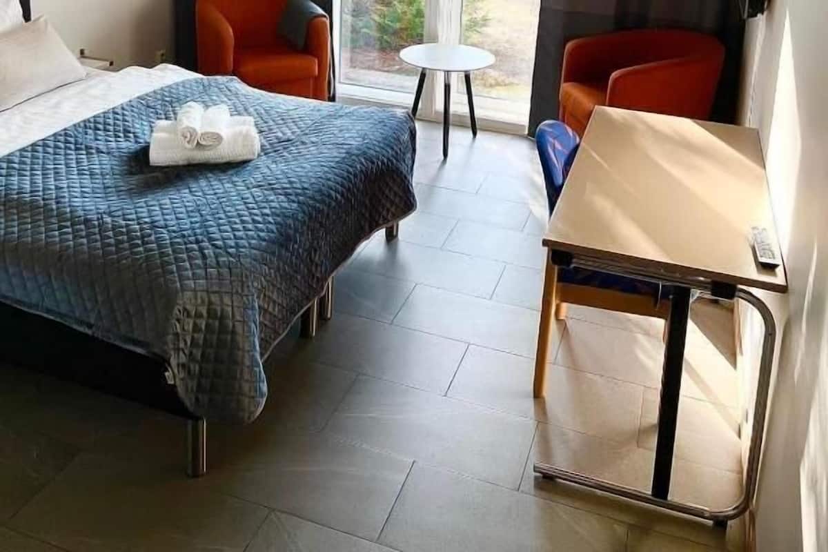 A hotel room with a bed, two chairs, a small table, and a view of the outdoors.