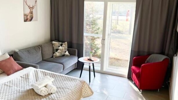 A modern hotel room with a bed, a grey sofa, a red armchair, and a small table. - Götaströms Värdshus (Skillingaryd)