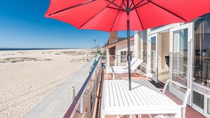 A beachside balcony with a red umbrella, overlooking a sandy beach and the ocean. - Oceanfront! Clean & Affordable Upstairs Split Level Unit (Newport Beach)