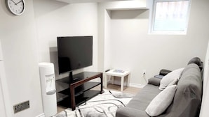 Una sala de estar moderna con un televisor de pantalla plana, un sofá, una mesita blanca y una alfombra estampada.