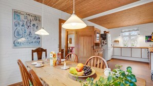 Una zona de menjador amb una taula de fusta, cadires i un plat de fruita. Hi ha una pissarra amb anotacions i un quadre a la paret.