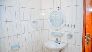Une salle de bain avec des carreaux blancs à motifs, un miroir rond, un lavabo sur pied et un porte-rouleau de papier toilette.