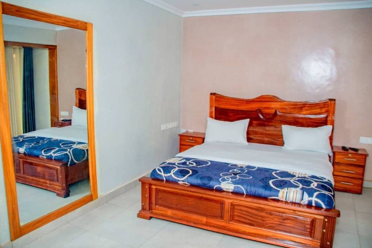 Een slaapkamer met een houten bed, nachtkastje, spiegel en een dressoir.