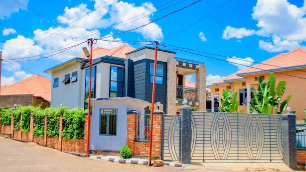 Une maison à deux étages dotée d’un balcon, d’une entrée sécurisée par un portail et d’un jardin bien entretenu.