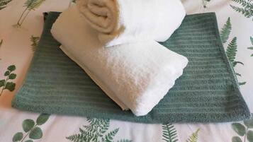 Ein ordentlich gefaltetes weißes Handtuch auf einem grünen Handtuch auf einem Bett mit einem botanischen Muster.
