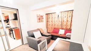 A compact living space with a sofa, a small table, and a kitchen area visible through an open door.