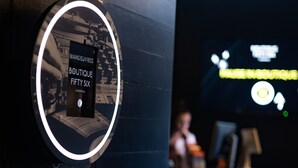Un panneau circulaire portant l’inscription « MANOEUVRES BOUTIQUE FIFTY SIX LIVERPOOL » et un écran numérique en arrière-plan.