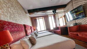Une chambre d’hôtel avec un grand lit, un canapé rouge, un téléviseur fixé au mur et un papier peint à motifs.