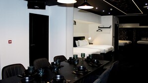 Une chambre d’hôtel moderne avec un coin repas, un lit avec du linge de maison blanc et un petit placard.
