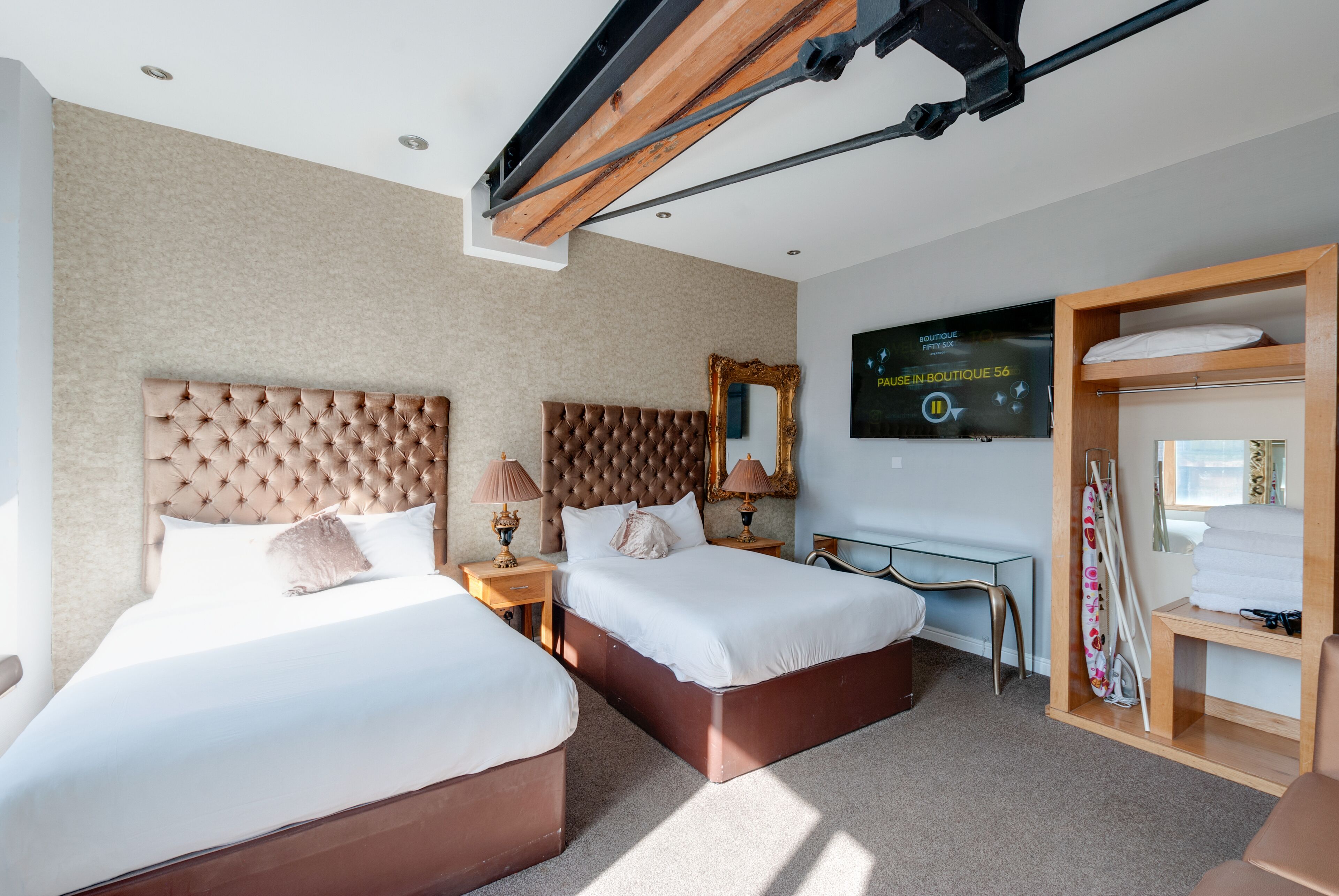 Ein Hotelzimmer mit zwei Betten, einem großen Spiegel, einem Flachbildfernseher und einem Holzschrank.
