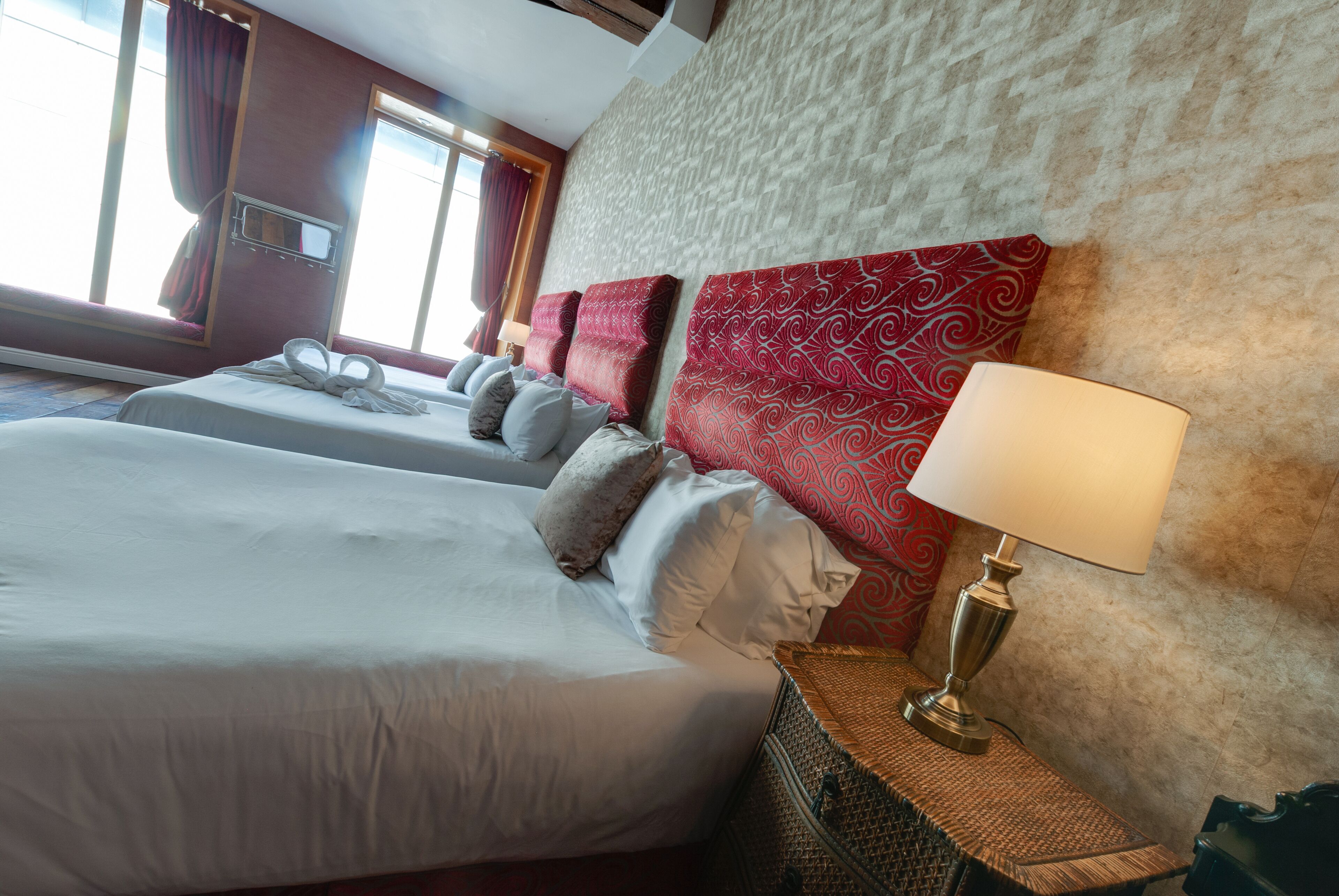 A hotel room with two beds, a large wall clock, and a lamp on a side table.