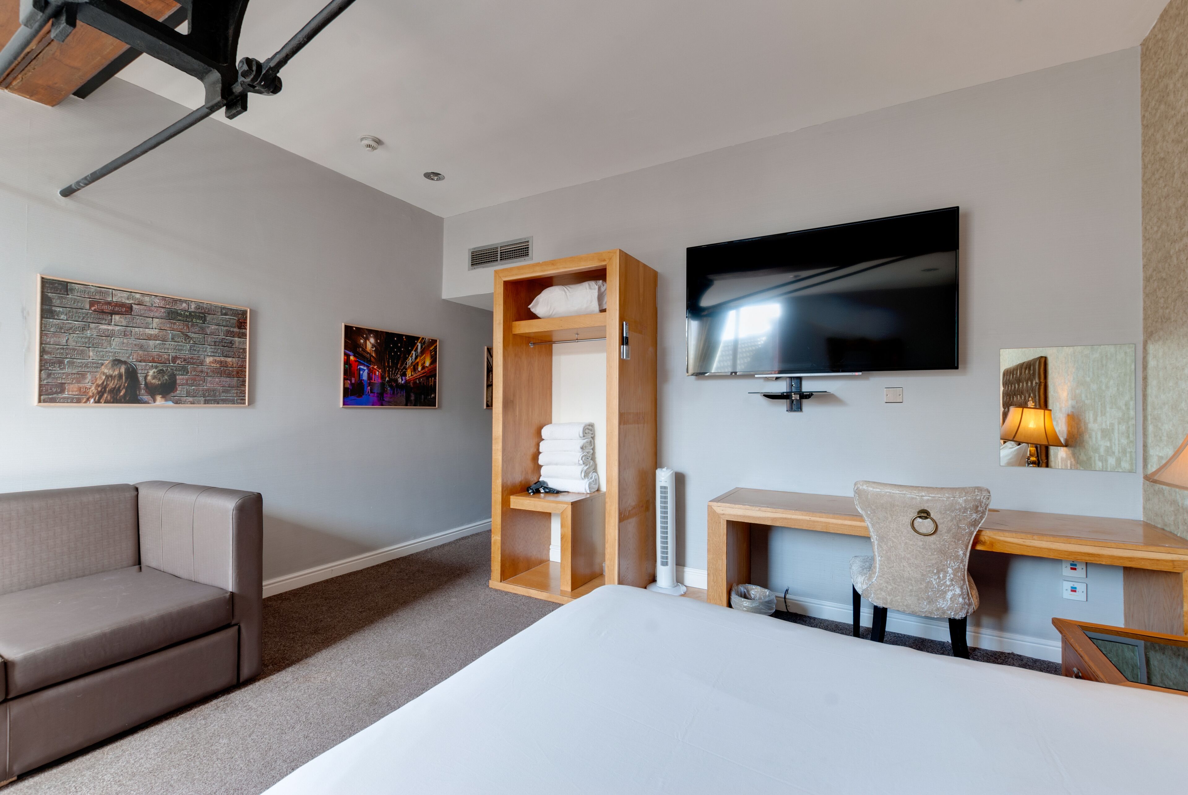 Una habitación de hotel moderna con cama, escritorio, silla, televisión y obras de arte en las paredes.