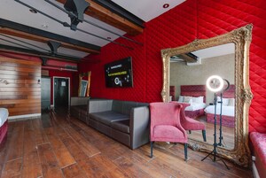 A hotel room with a red quilted wall, a large ornate mirror, a grey sofa, and a pink armchair.
