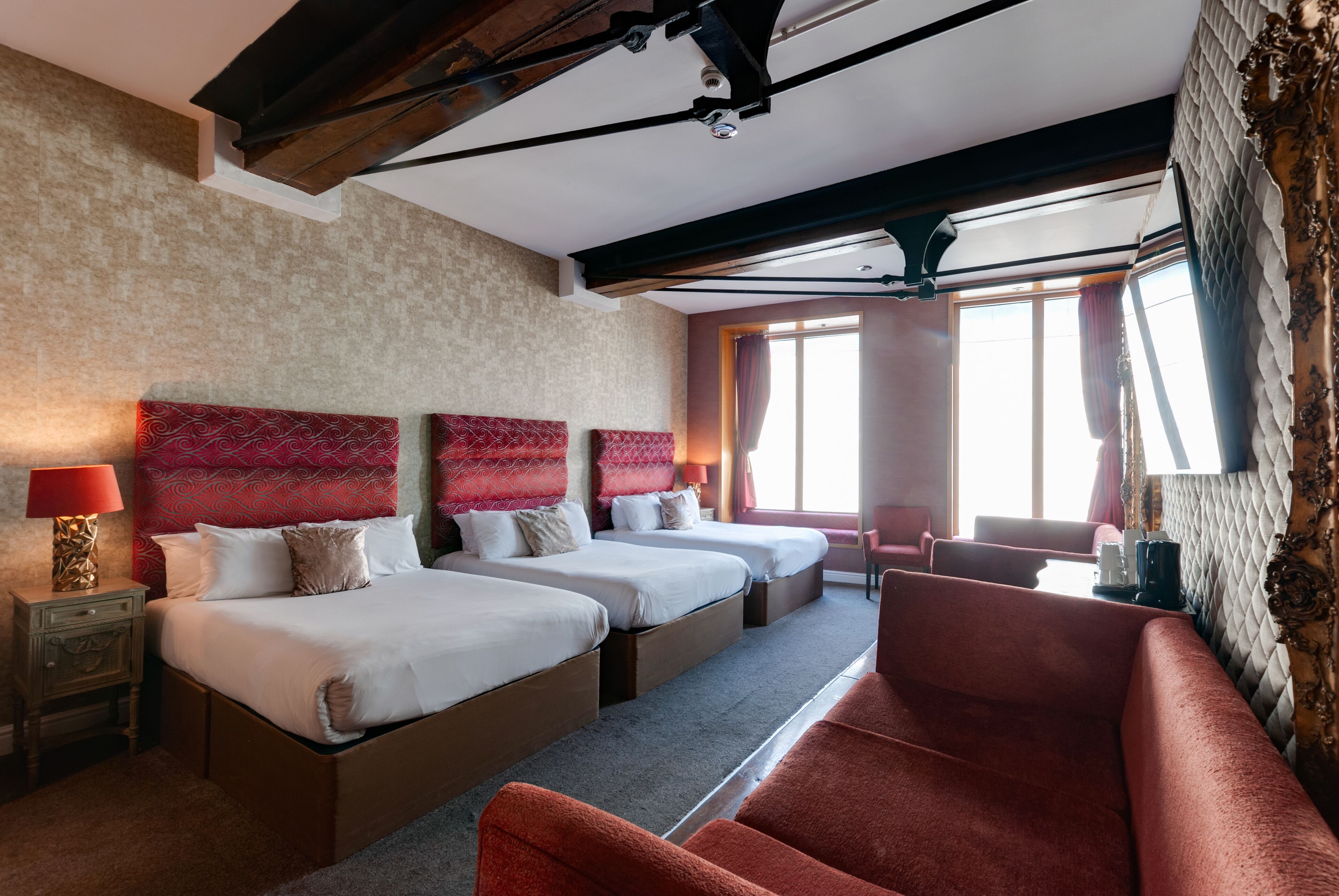 Une chambre d’hôtel avec deux lits, un canapé rouge, une table de chevet avec une lampe et une grande fenêtre avec des rideaux.