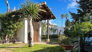 Eine Steinsäule, eine Holzpergola und ein kleines Gebäude mit weißer Fassade.