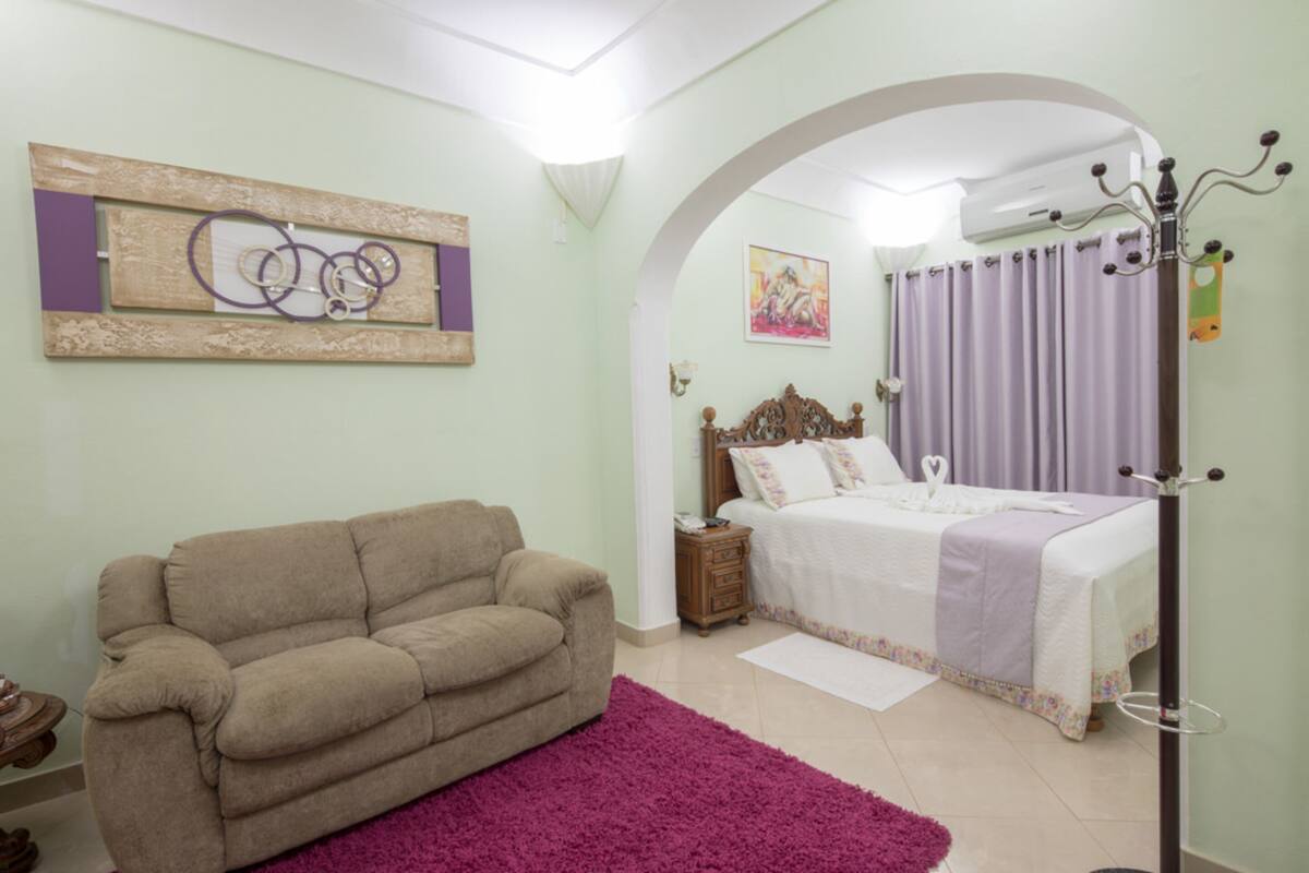 Um quarto com uma cama, um sofá, uma mesa de cabeceira, um espelho e uma obra de arte na parede.