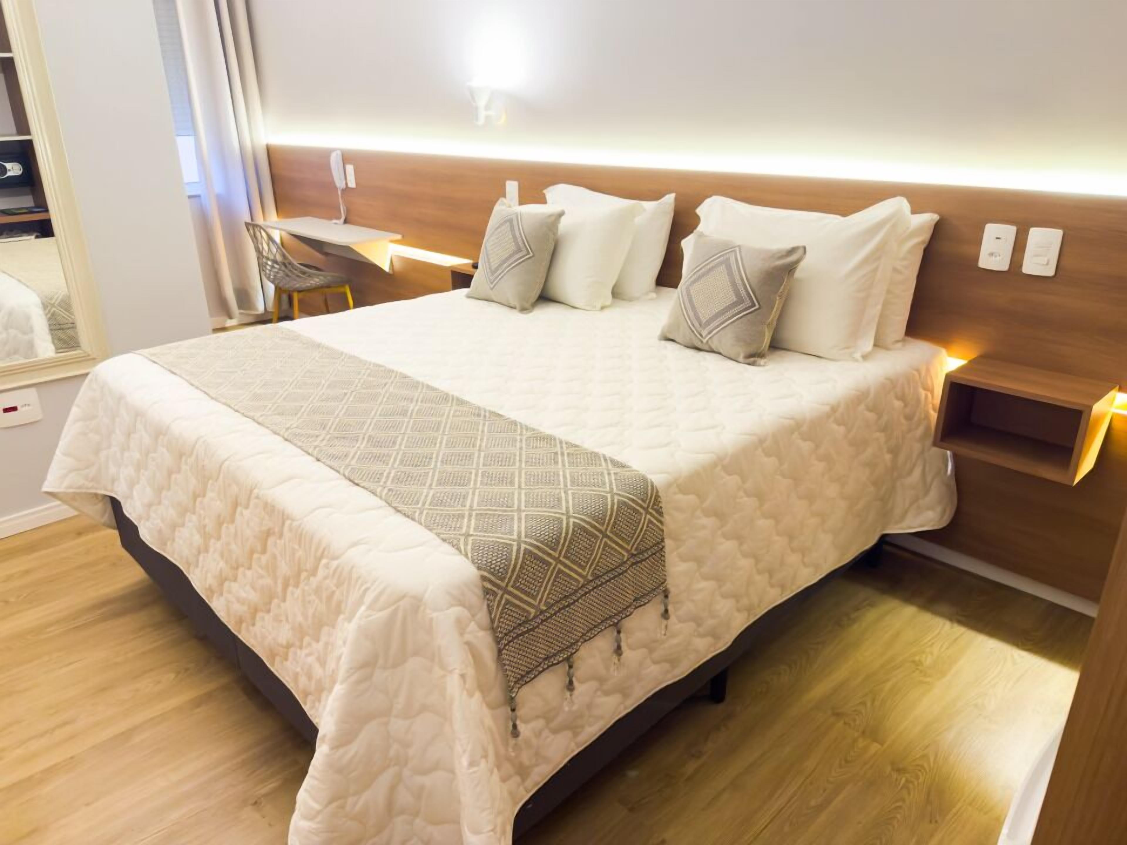 Una cama bien hecha con una colcha acolchada, una mesita de noche con una lámpara y un aplique de pared.