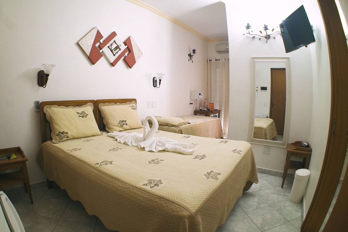 Quarto de hotel com duas camas, um espelho, uma televisão e uma mesinha.