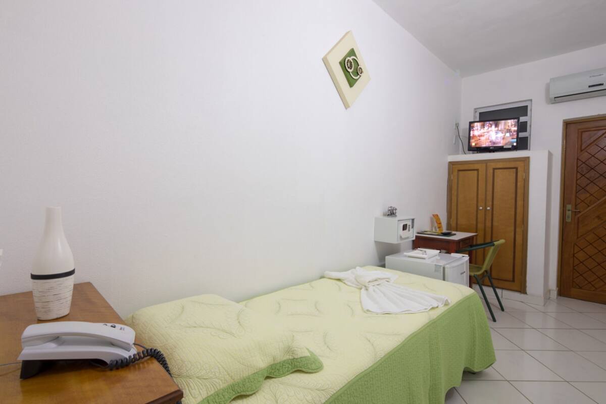 Quarto com cama, escrivaninha com telefone, cadeira, televisão, armário e porta.