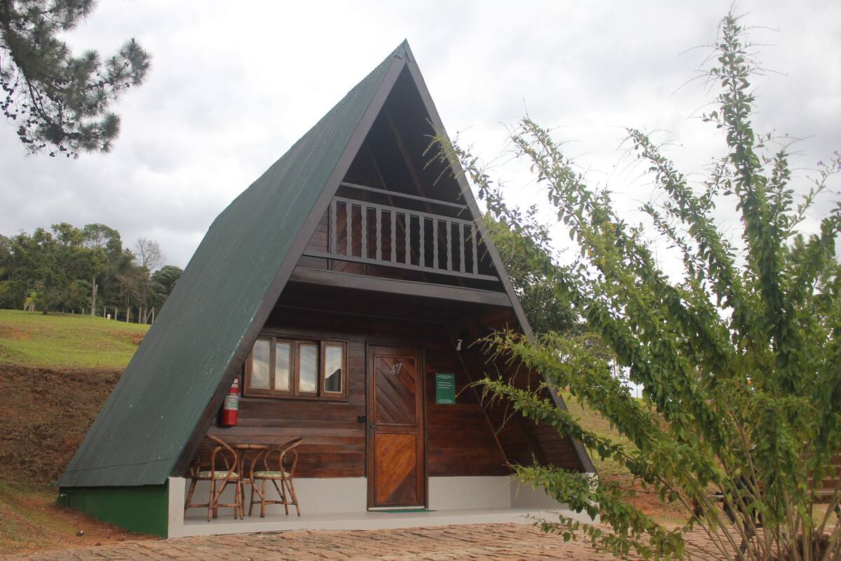 Uma cabana de madeira triangular com varanda, porta e janela.