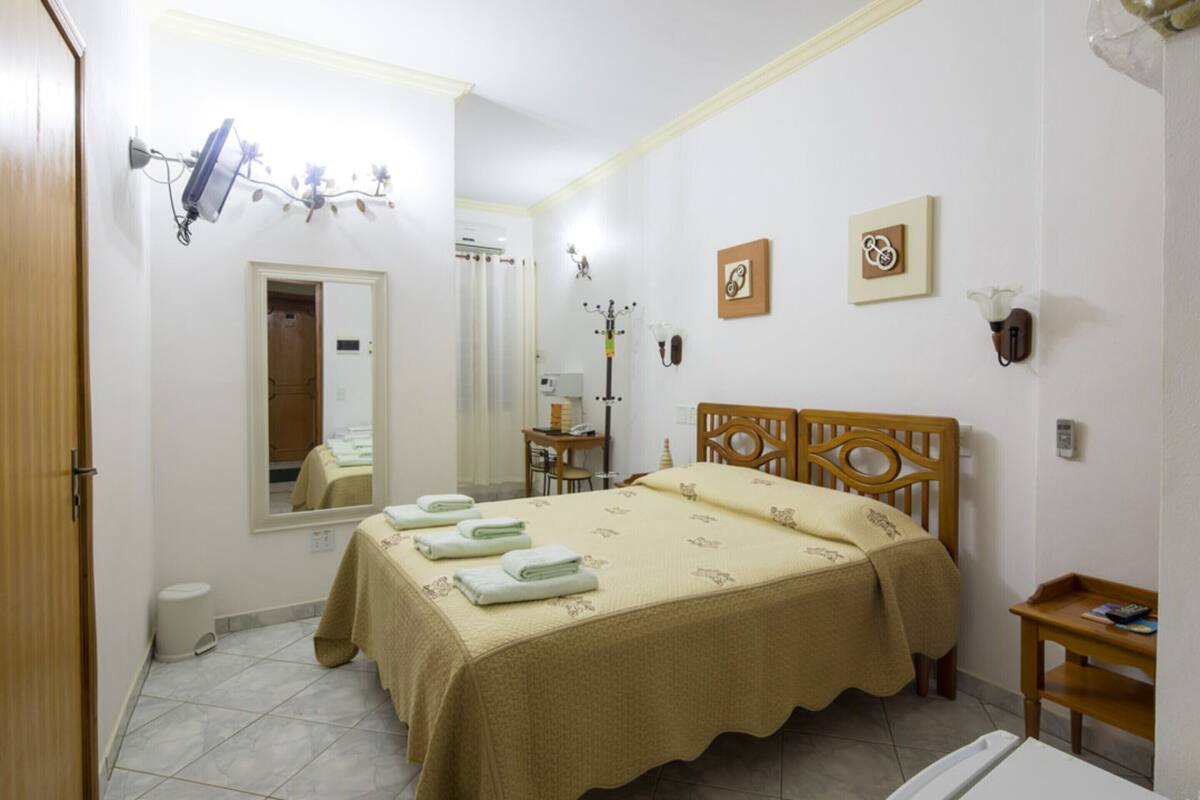 Quarto com cama, espelho, mesa de cabeceira, cadeira e uma pequena mesa com abajur.