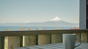 A view of a mountain from a balcony with a white mug on the table. - Loft Boutique "Ave Lodge" in Frutillar - 1 (Frutillar)