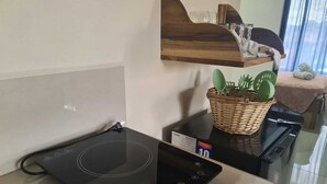 A kitchen with a black induction cooktop, a wicker basket with kitchen utensils, and a wooden shelf above. - New apartment 5 minutes from the central park (La Fortuna)