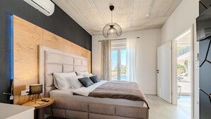 A modern bedroom with a large bed, a bedside table, a lamp, and a view of the outdoors.