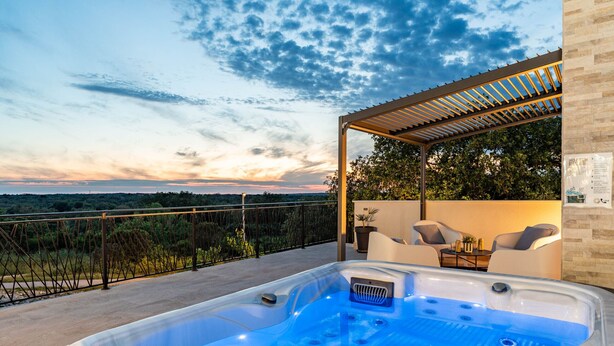 A hot tub with a view of the sunset and a pergola with seating.