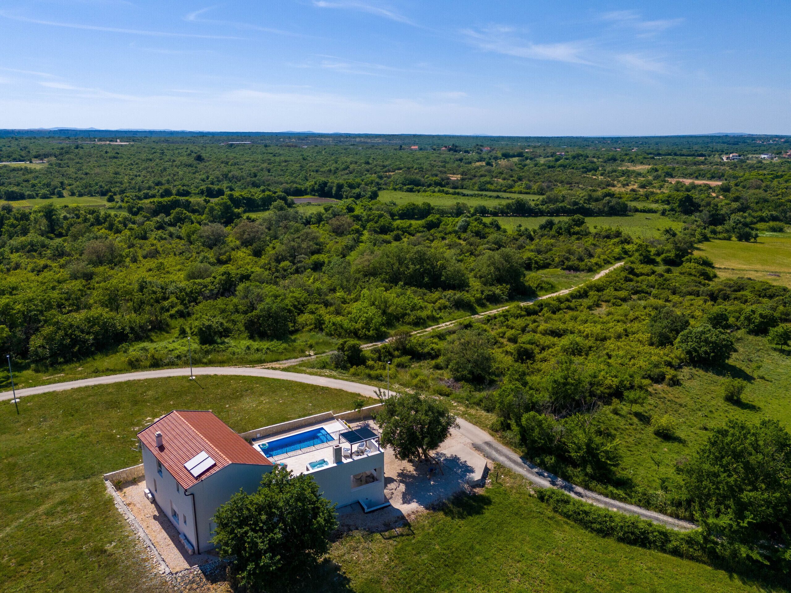 Una casa con piscina, rodeada de abundante vegetación y un cielo despejado.