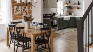 A modern kitchen with dark cabinets, a wooden dining table, and a staircase. - Secluded Valley Oasis with Swimming Pond, Spa, Firepit, 3BD/2BA, Family friendly (Liverpool)