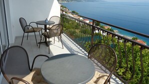 Een balkon met een tafel en stoelen, met uitzicht op de kust en bergen in de verte.