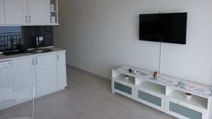 Een moderne keuken met witte kasten, een zwart aanrecht en een inbouwfornuis. Een flatscreen-tv is bevestigd aan de muur boven een wit tv-meubel met lades.