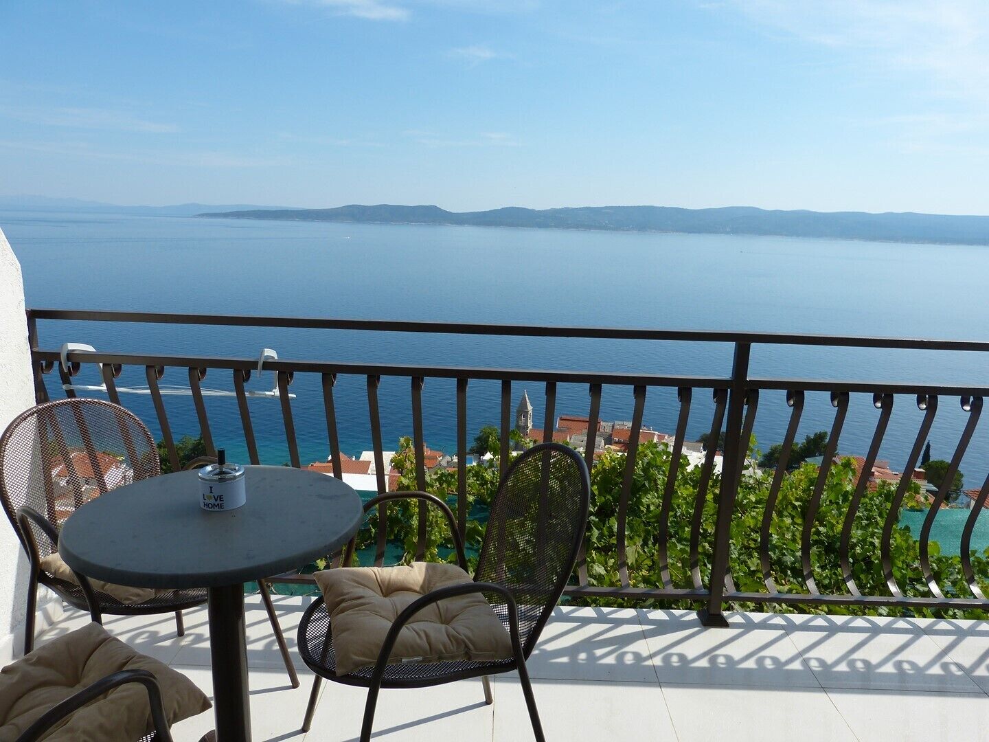 Un balcon avec une table et des chaises, donnant sur une étendue d’eau et sur une terre lointaine.