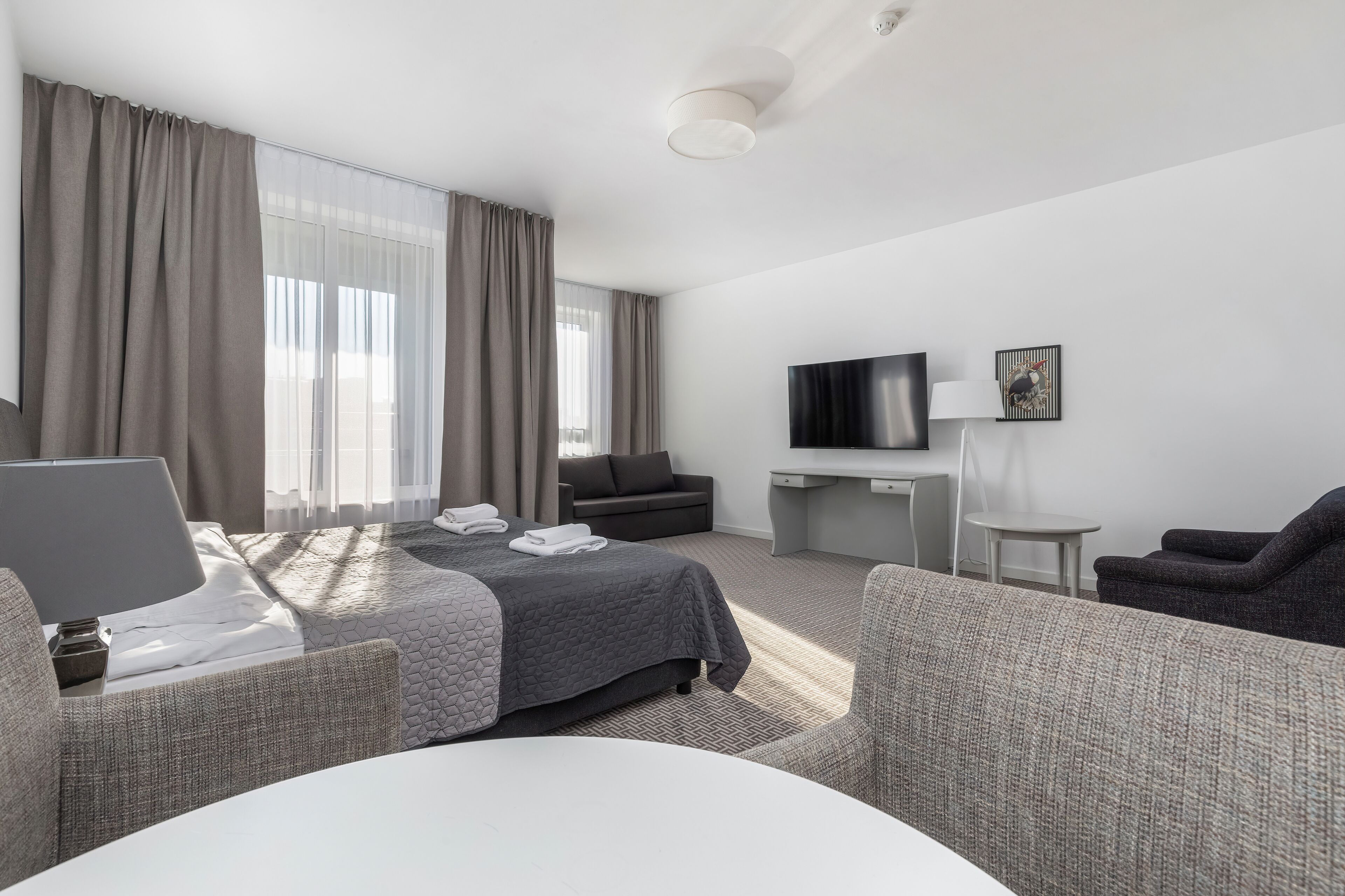 A hotel room with a bed, a desk, a TV, and a seating area.
