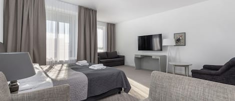 A hotel room with a bed, a desk, a TV, and a seating area.
