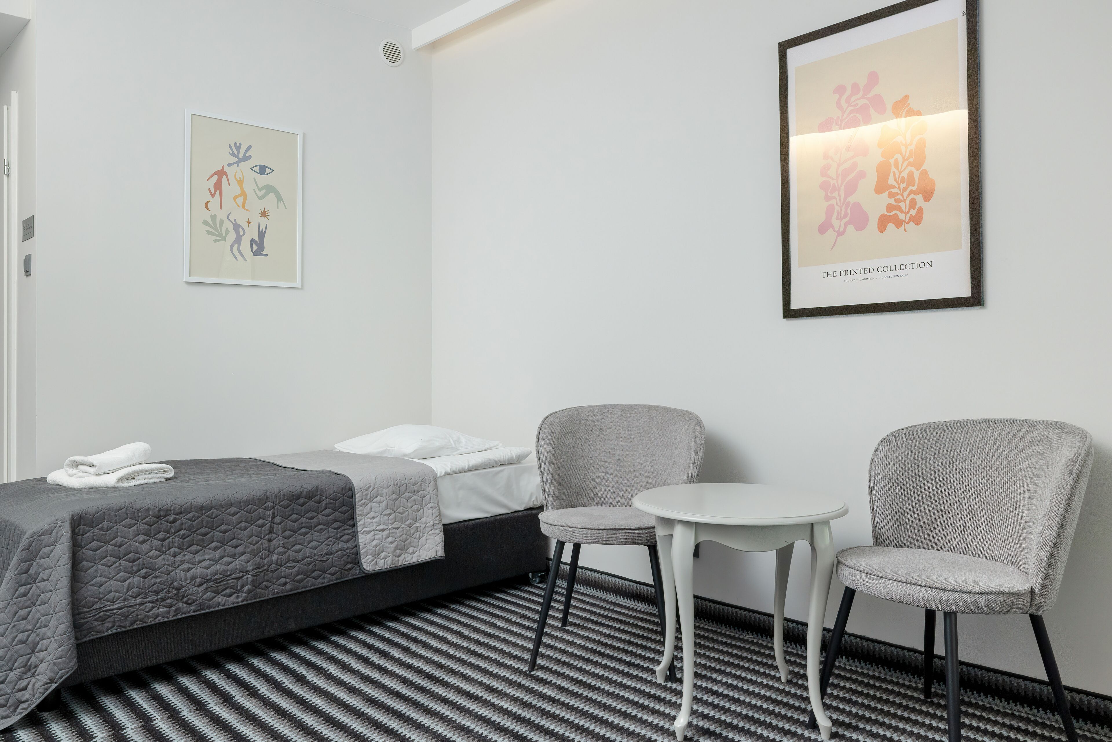 Ein Hotelzimmer mit einem Bett, zwei Sessel, einem kleinen Tisch und zwei Wandbildern.