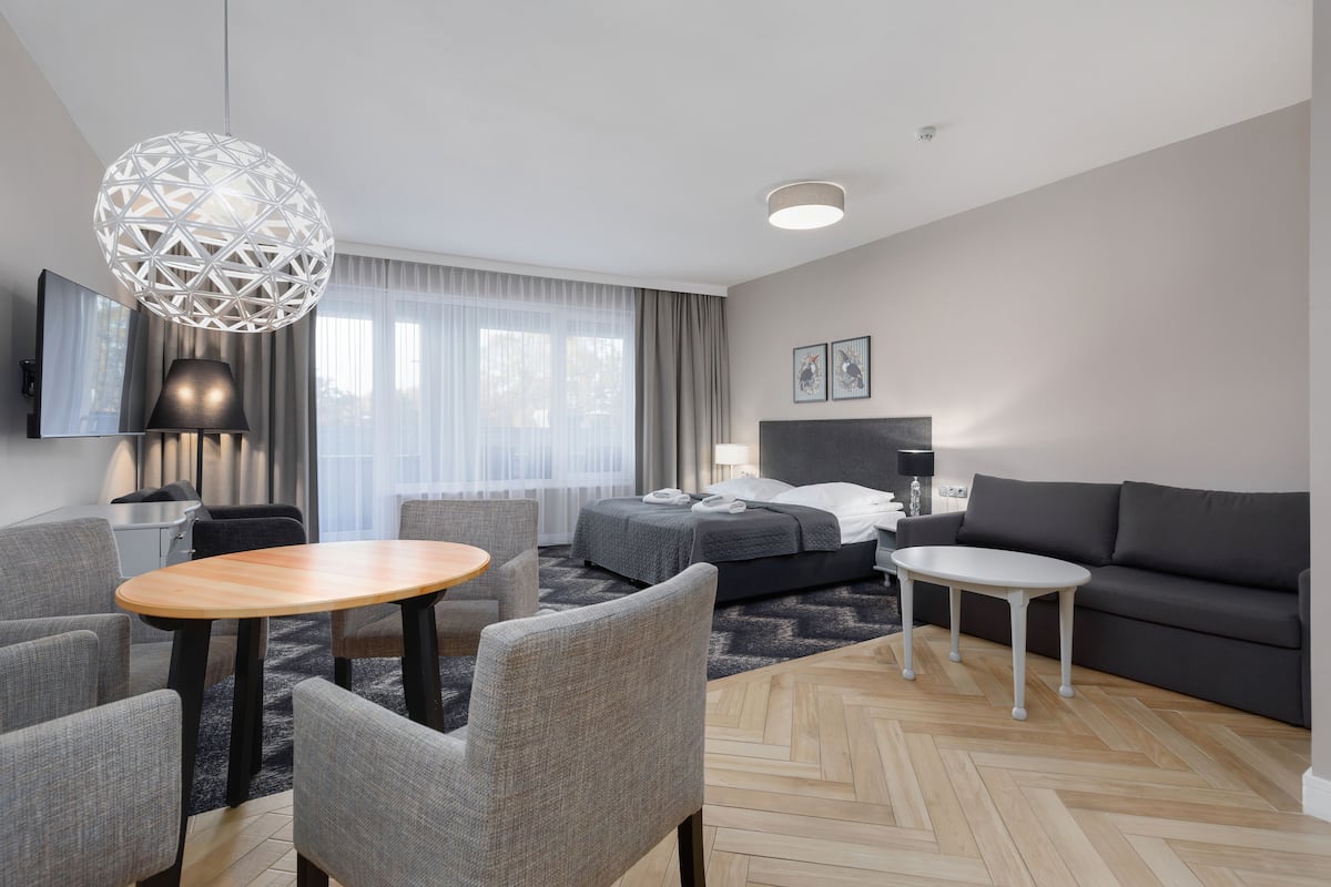 Een moderne hotelkamer met een bed, bank, eettafel, stoelen en een grote decoratieve lamp.