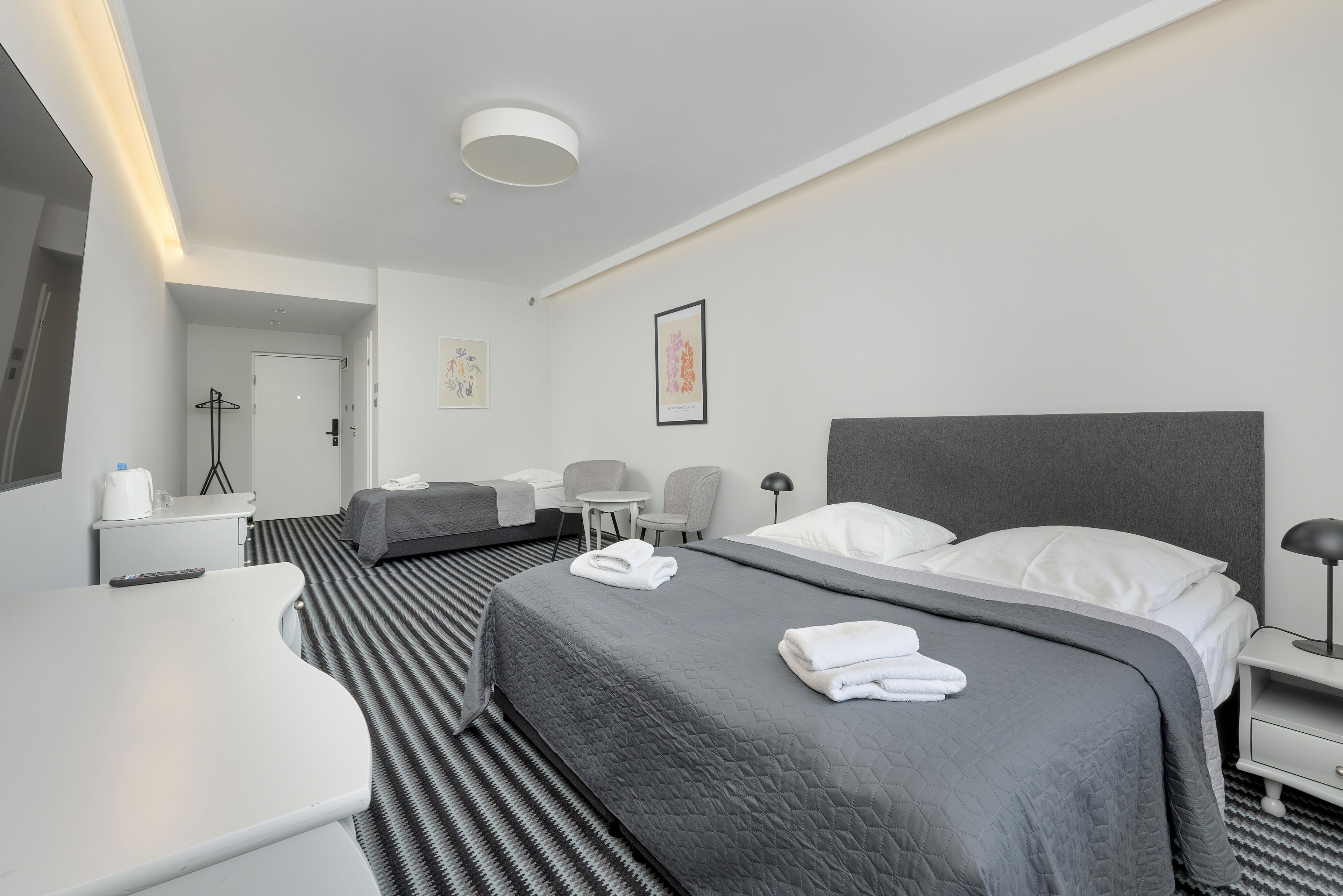 A modern hotel room with a large bed, a desk, a chair, and a small table.