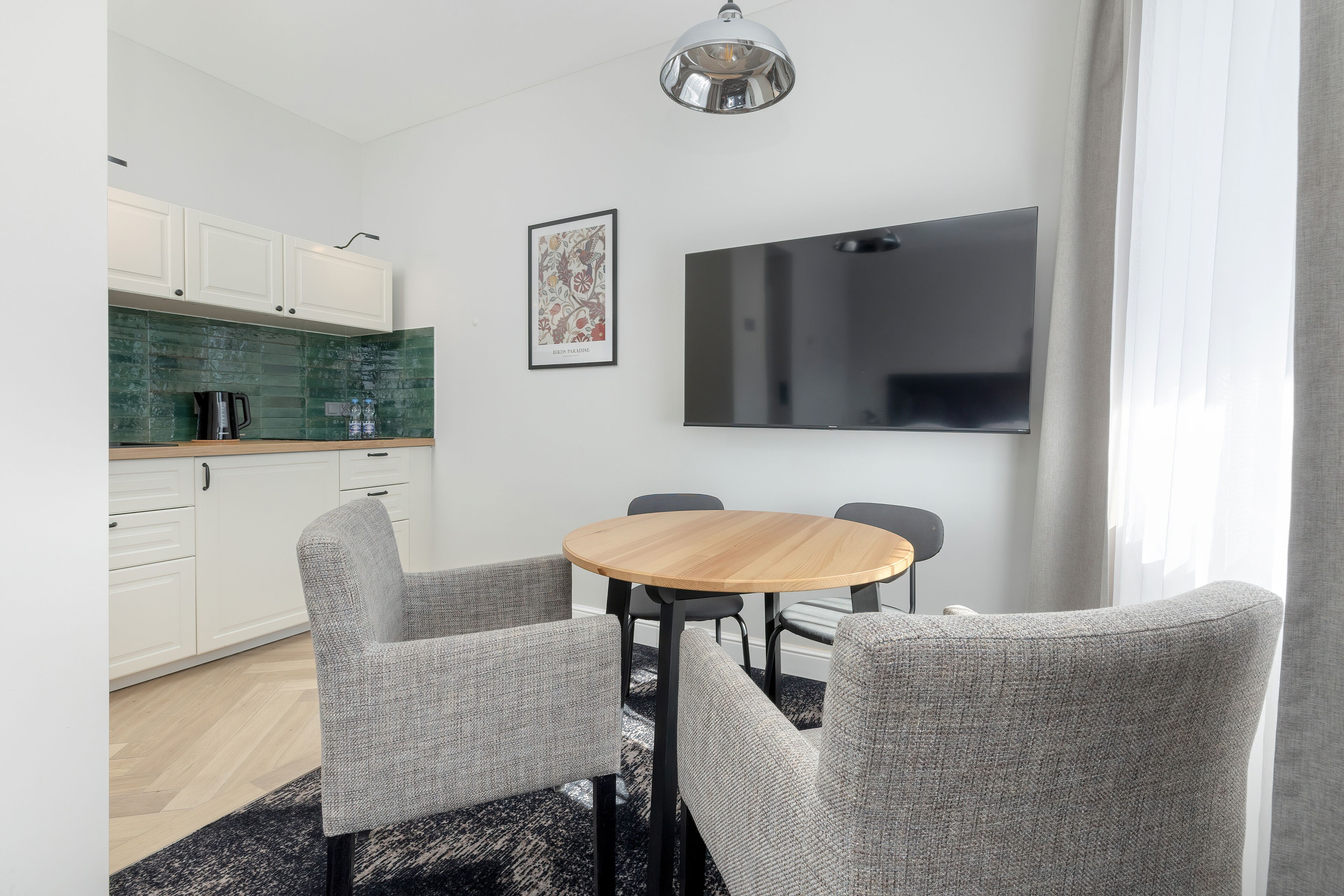 A modern kitchen with white cabinets, a green backsplash, and a round wooden table with four grey upholstered chairs.