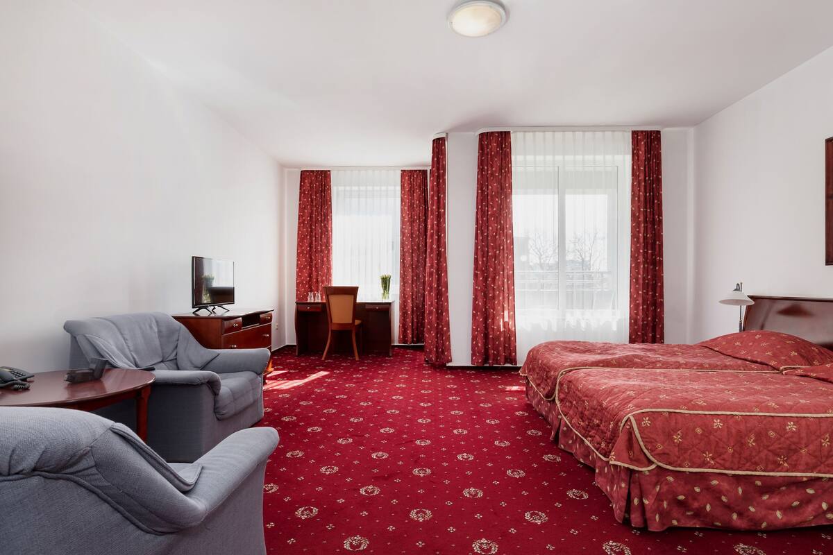 Een hotelkamer met een roodgekleurd tapijt, twee bedden, een bureau met stoel, een bank en een televisie.