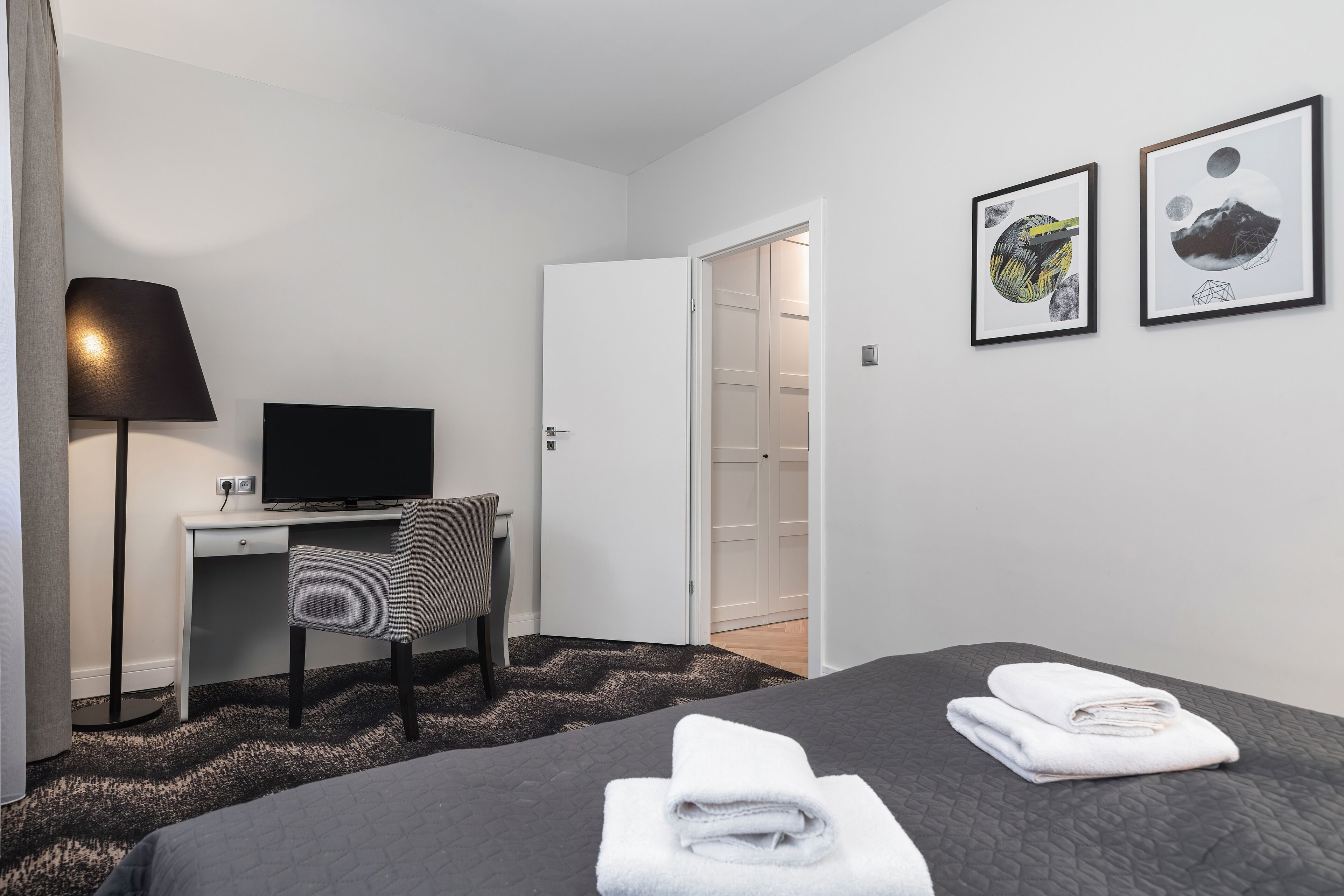 A hotel room with a bed, a desk with a chair, a television, and artwork on the wall.