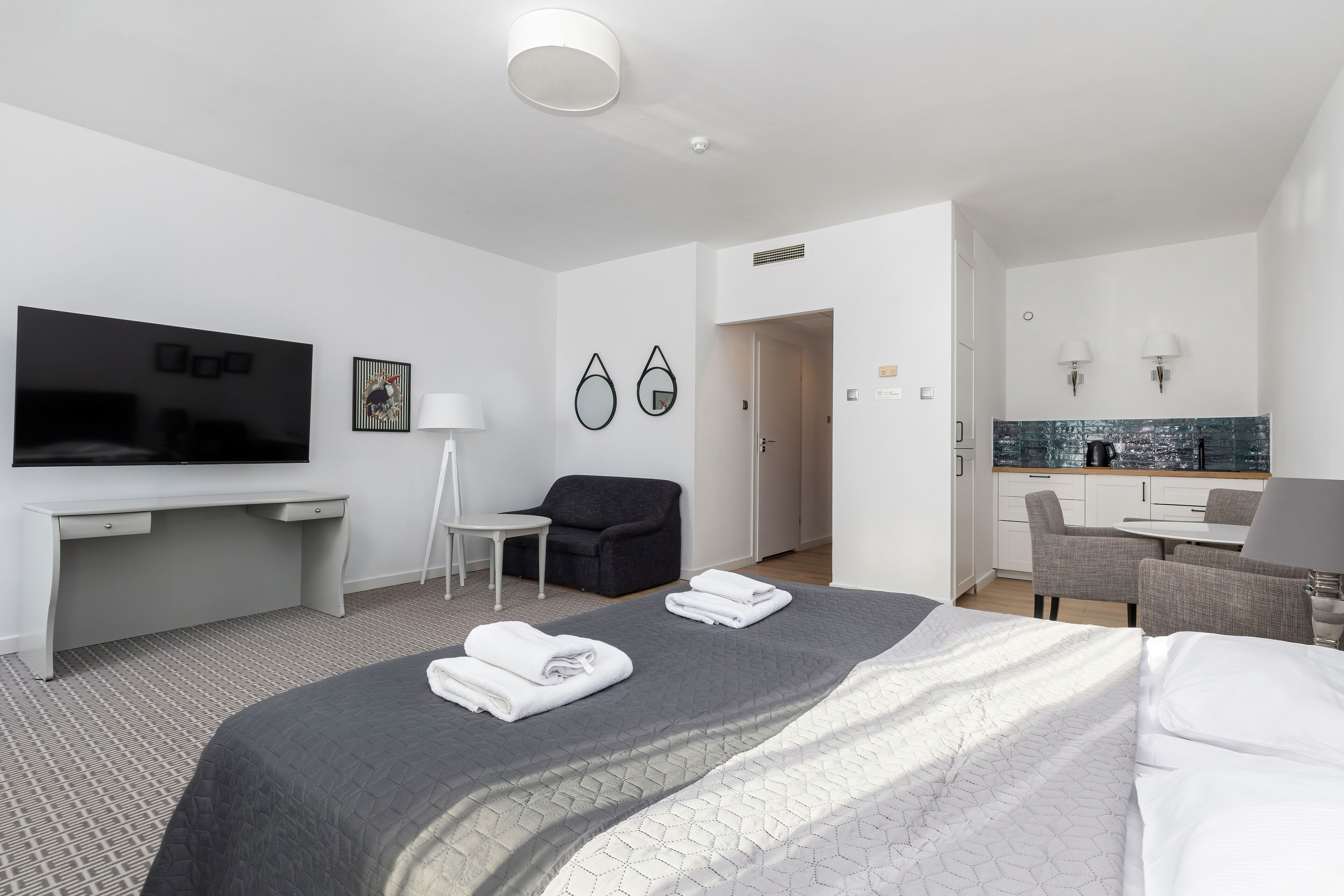 A modern hotel room with a large bed, a desk, a flat-screen TV, a chair, and a small table.