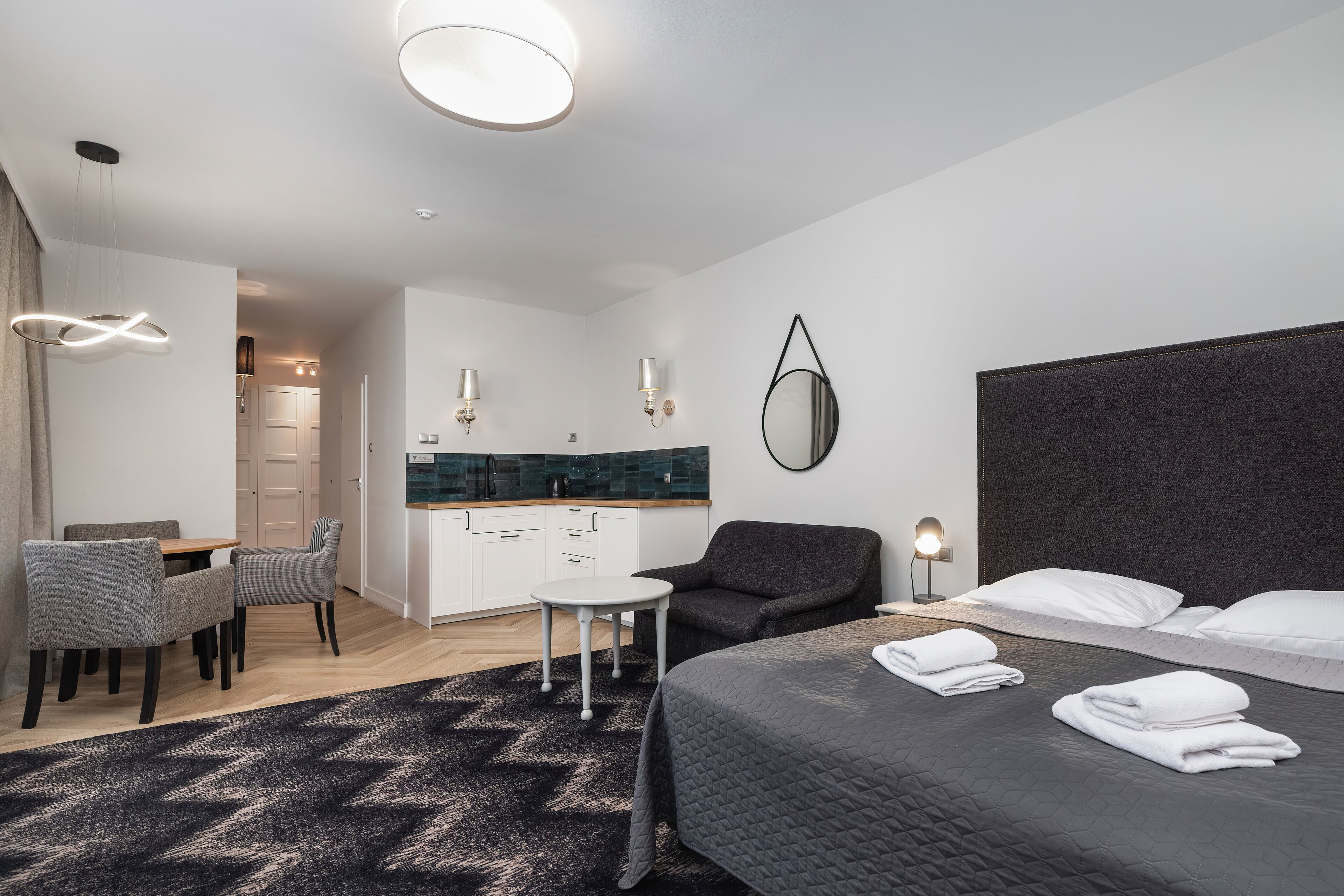 Una habitación de hotel moderna con una cama grande, un escritorio pequeño, una silla, una mesa redonda y una kitchenette.