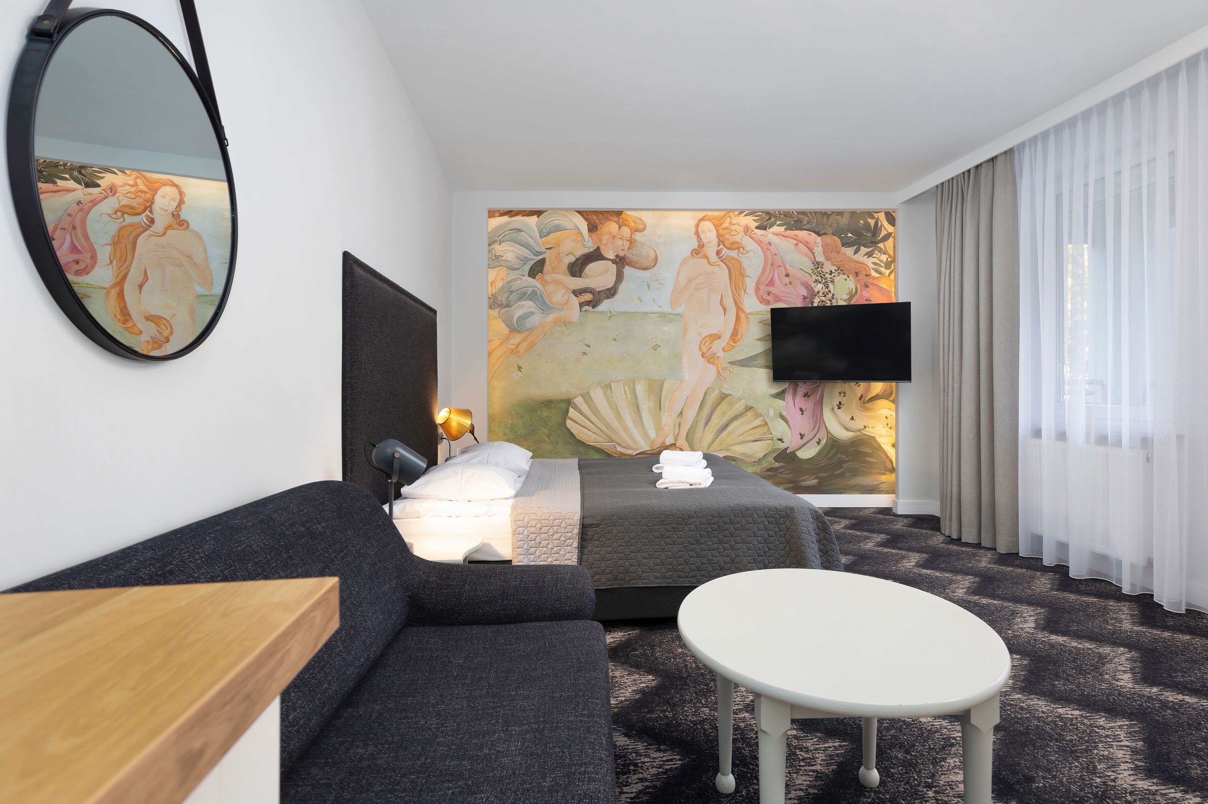 Habitación de hotel con una cama grande, un sofá, una mesita, un televisor de pantalla plana y un mural en la pared.