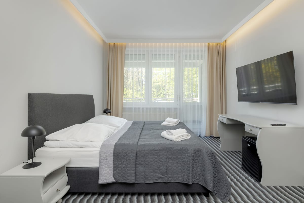 Een moderne hotelkamer met een bed, een bureau, een stoel, een televisie en een raam met gordijnen.